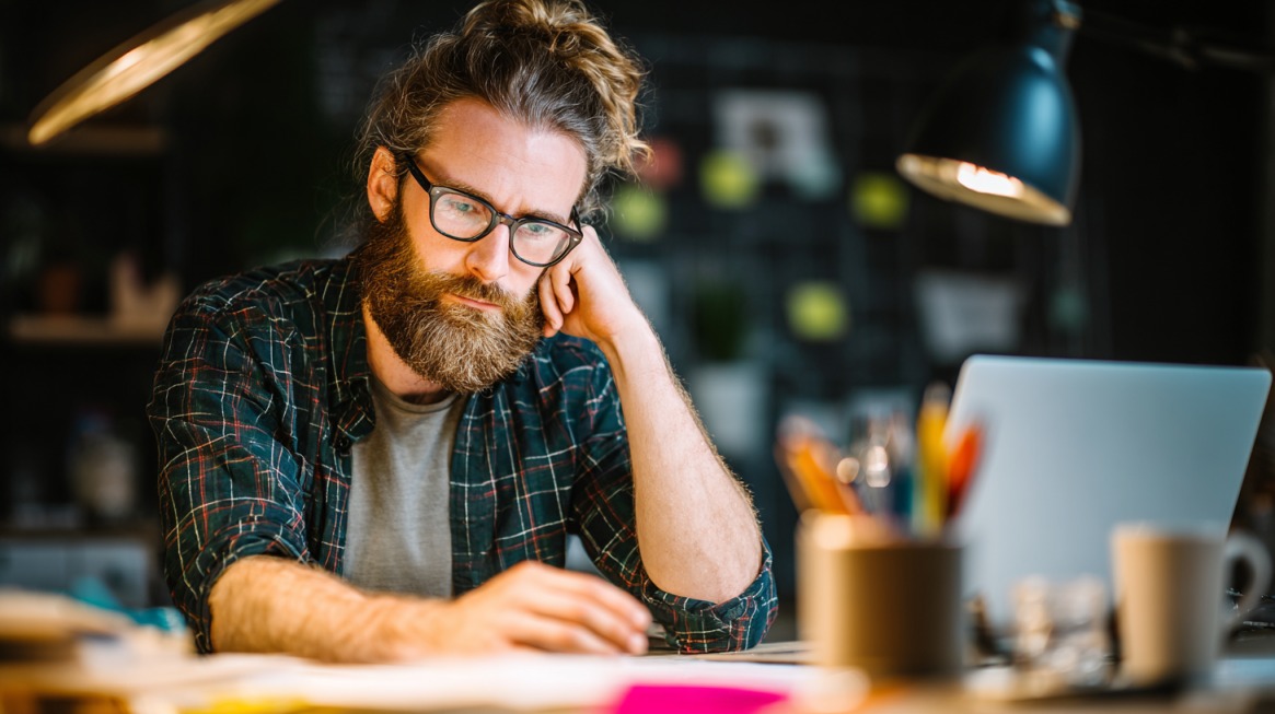 Man working at a desk with a laptop while leaning forward and resting his head on his hand