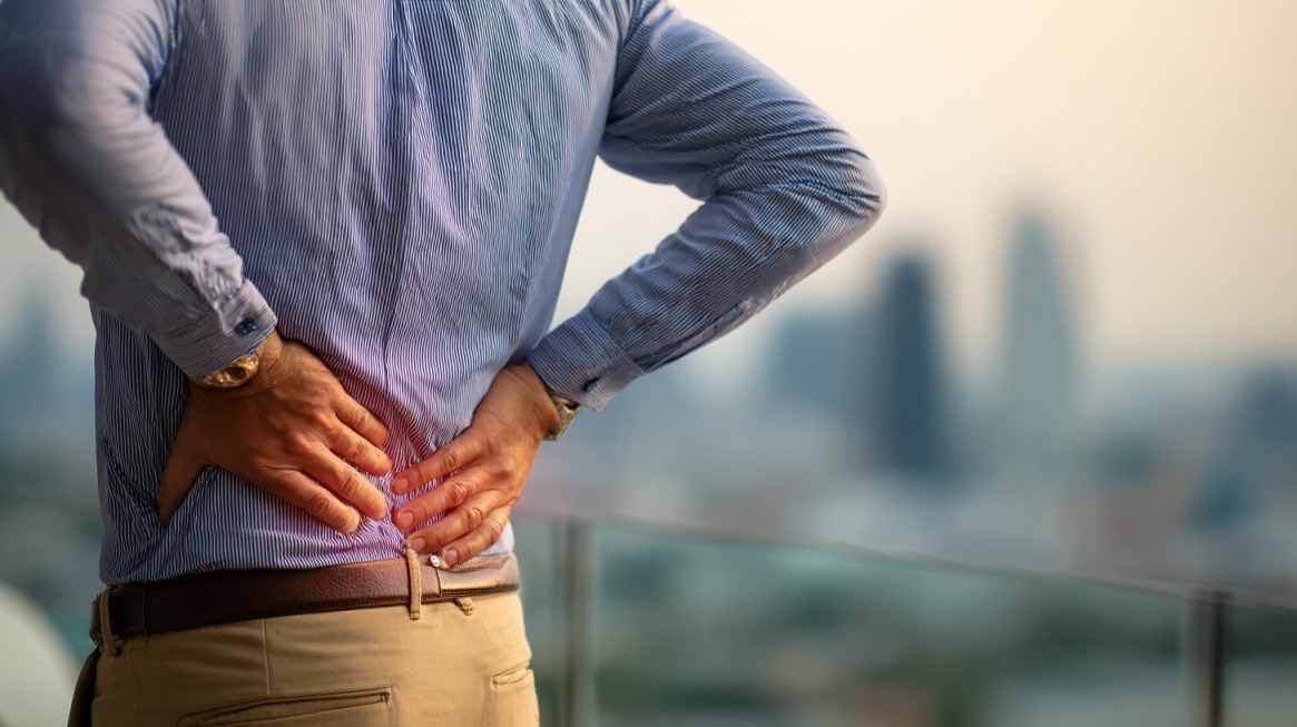 Person standing outdoors holding their lower back with a city skyline in the background