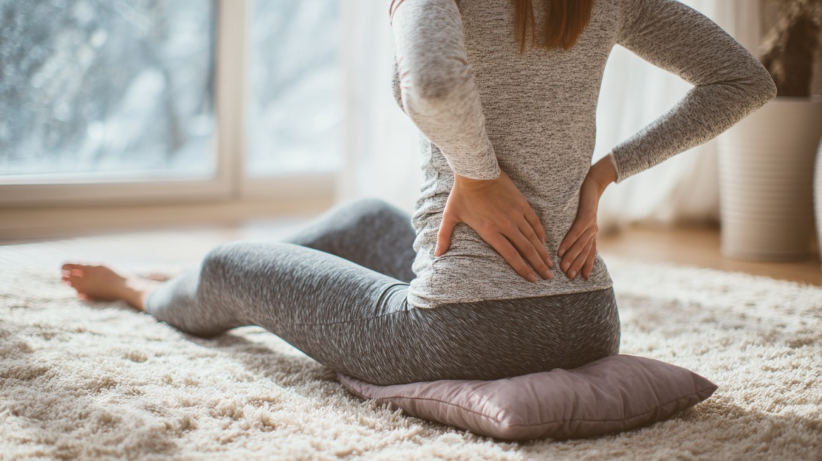 Person sitting on a cushion while holding their lower back in a bright room